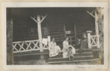 Members of the Hartley family sitting on the front porch of the cabin at the maple sugar camp in Trout Lake