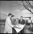 Four people looking at blueprints at the construction site of University Circle at UMD