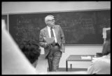 An instructor standing in front of a chalkboard in the School of Business and Economics at UMD