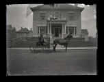 Mrs. Hubbard seating in buggy on the road outside of a house