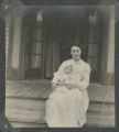 Mary Rogers sitting on the front steps of a house with a baby in her lap