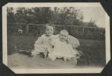 Child and a baby sitting on a blanket in the front yard of a house