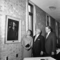 Three people standing and looking at a portrait of Richard L. Griggs in the UMD Campus Club