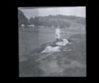 Girls lying in a field, one girl, standing, overlooks them