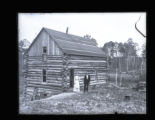 Mr. Cummings's log home, with Mr. and Mrs. Cummings standing in front of it