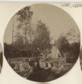 Person sitting on a bench with someone standing above them holding a child beside the creek near the Hartley house at 1305 East Superior Street