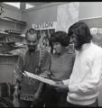 Three students viewing a poster for the 1975 Feast of Nations event at UMD