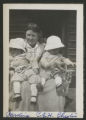 Carrie Eliza Hartley sitting in a chair with Caroline Claypool and Chester Adgate Congdon II in her lap on the front porch of the cabin at the maple sugar camp in Trout Lake