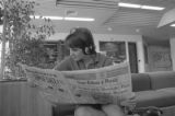 Student wearing headphones and reading newspaper in Kirby Student Center lounge