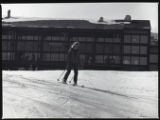 Action shot of UMD 1979 women's downhill skier in front of ski lodge