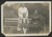 Carrie Eliza Hartley standing behind Rebecca Barker Hartley and an unidentified child sitting on a bench outside of the Hartley house at 1305 East Superior Street