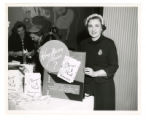 Blossom Meshbesher stands next to a sign for the "Everyone Can Cook" cookbook fundraiser for the Mount Sinai Women's Auxiliary, Minneapolis, Minnesota