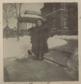 Judith Hartley standing with a miniature baby carriage on a walkway in front of the Hartley house at 1305 East Superior Street