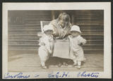 Carrie Eliza Hartley sitting in a chair with Caroline Claypool and Chester Adgate Congdon II standing beside her on the front porch of the cabin at the maple sugar camp in Trout Lake